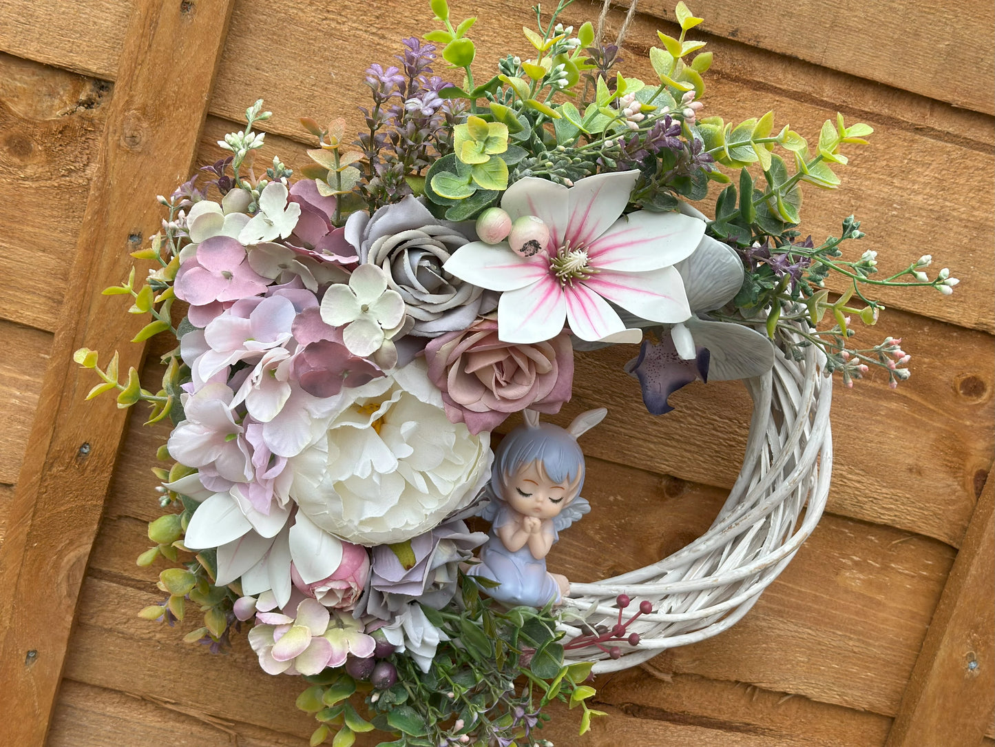 Romantic floral wreath with artificial pink, white, and grey flowers, accented with greenery and an angel figurine. Ideal for spring and Easter.