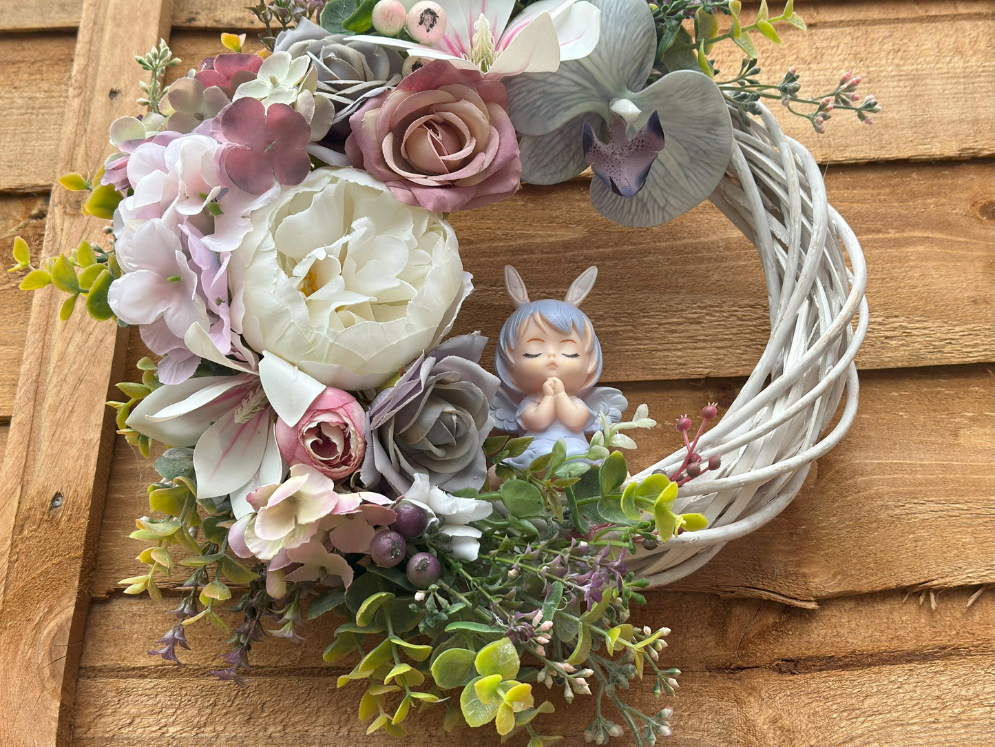 Elegant handmade wreath with soft roses, hydrangeas, and orchids, complemented by a praying angel. A charming addition to any door or wall.