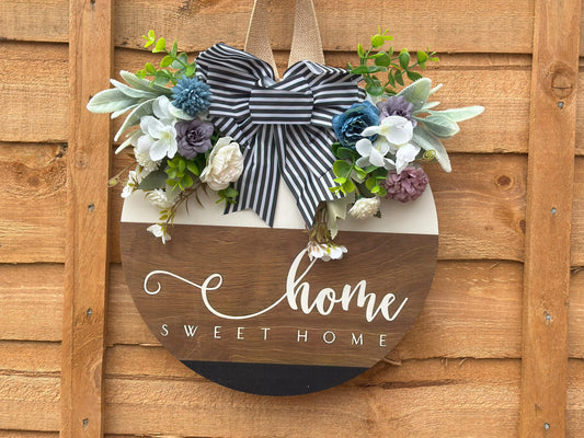 Handmade wooden wreath with artificial flowers and striped fabric bow, "Home Sweet Home" sign, rustic farmhouse door decor, modern classic wall hanging, cozy home decoration, indoor and outdoor wreath, neutral white and light brown tones.